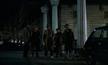 Movie still from “The Professional” (1981), directed by Georges Lautner – A group of people standing next to each other on a street; Wide shot, Low angle