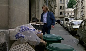 Movie still from “The Professional” (1981), directed by Georges Lautner – A man walking down a street near a pile of trash; Wide shot, High angle
