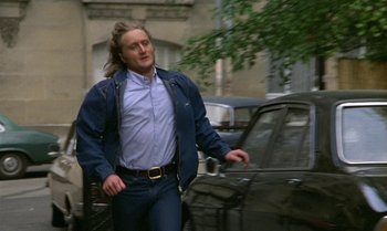 Movie still from “The Professional” (1981), directed by Georges Lautner – A man with long hair is walking down the street; Medium shot, Low angle