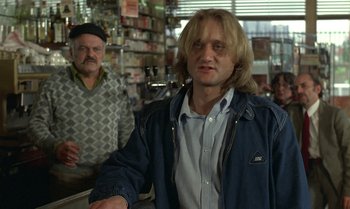 Movie still from “The Professional” (1981), directed by Georges Lautner – A man standing next to another man in a store; Medium shot, Over the shoulder angle