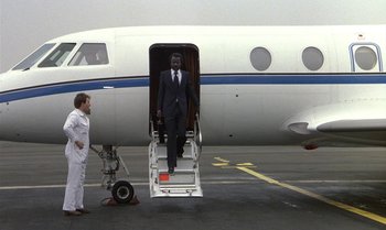 Movie still from “The Professional” (1981), directed by Georges Lautner – A man in a suit is stepping off of an airplane; Wide shot, Low angle