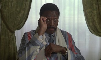 Movie still from “The Professional” (1981), directed by Georges Lautner – A man in a striped shirt holding his glasses up; Close Up shot, High angle