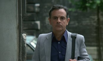 Movie still from “The Professional” (1981), directed by Georges Lautner – A man in a gray jacket and a blue shirt holding an umbrella; Close Up shot, Over the shoulder angle