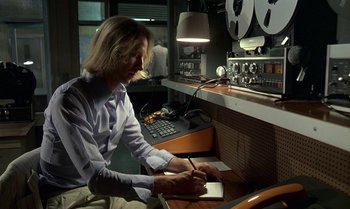 Movie still from “The Professional” (1981), directed by Georges Lautner – A man writing on a piece of paper in front of a desk; Medium shot, High angle