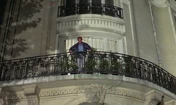 Movie still from “The Professional” (1981), directed by Georges Lautner – A man standing on the balcony of a building; Wide shot, Low angle