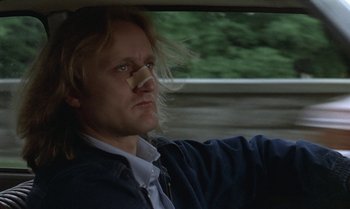 Movie still from “The Professional” (1981), directed by Georges Lautner – A man in a blue jacket sitting in the back of a car; Close Up shot, Low angle