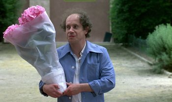 Movie still from “The Professional” (1981), directed by Georges Lautner – A man in a blue jacket holding a pink umbrella; Medium shot, Over the shoulder angle