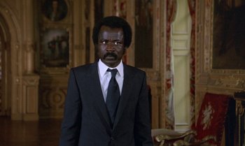 Movie still from “The Professional” (1981), directed by Georges Lautner – A man in a suit and tie standing in front of a painting; Medium shot, Low angle