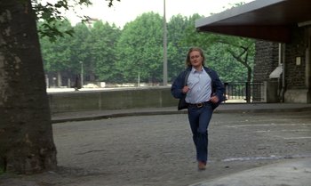 Movie still from “The Professional” (1981), directed by Georges Lautner – A man walking on the sidewalk in a park; Wide shot, High angle
