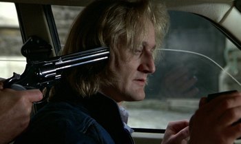 Movie still from “The Professional” (1981), directed by Georges Lautner – A man in a car looking at his cell phone; Close Up shot, Over the shoulder angle