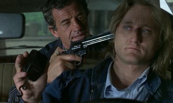 Movie still from “The Professional” (1981), directed by Georges Lautner – A man holding a gun pointed at another man in the back of a car; Close Up shot, Over the shoulder angle