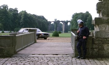 Movie still from “The Professional” (1981), directed by Georges Lautner – A police officer standing on a bridge in a park; Wide shot, Over the shoulder angle