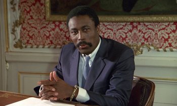 Movie still from “The Professional” (1981), directed by Georges Lautner – A man sitting at a table wearing a suit and tie; Close Up shot, Low angle