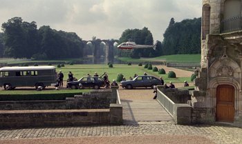 Movie still from “The Professional” (1981), directed by Georges Lautner – A group of people standing around cars in a park; Extreme Wide shot, High angle