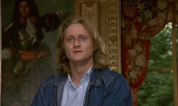 Movie still from “The Professional” (1981), directed by Georges Lautner – A man with long blonde hair wearing a blue jacket; Close Up shot, Low angle