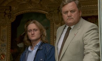 Movie still from “The Professional” (1981), directed by Georges Lautner – A man standing next to another man in a suit; Close Up shot, Low angle