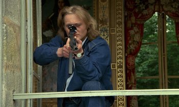 Movie still from “The Professional” (1981), directed by Georges Lautner – A man holding a gun while standing on top of a building; Medium shot, Low angle