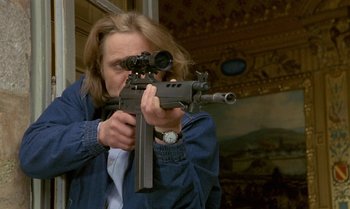 Movie still from “The Professional” (1981), directed by Georges Lautner – A man is holding a rifle and aiming it; Medium shot, Low angle