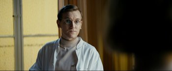 Movie still from “Journal 64” (2018), directed by Christoffer Boe – A man wearing a white lab coat and round glasses; Close Up shot, Over the shoulder angle