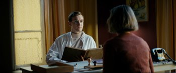 Movie still from “Journal 64” (2018), directed by Christoffer Boe – A man in a white lab coat holding a book; Medium shot, Over the shoulder angle