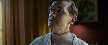 Movie still from “Journal 64” (2018), directed by Christoffer Boe – A man wearing glasses and a white shirt; Close Up shot, Low angle