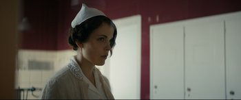 Movie still from “Journal 64” (2018), directed by Christoffer Boe – A woman wearing a nurse's hat in front of a red wall; Close Up shot, Low angle
