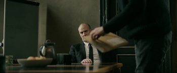 Movie still from “Journal 64” (2018), directed by Christoffer Boe – A man sitting at a table in front of another man; Medium shot, Over the shoulder angle
