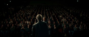 Movie still from “Journal 64” (2018), directed by Christoffer Boe – A group of people sitting in front of an audience; Wide shot, Over the shoulder angle