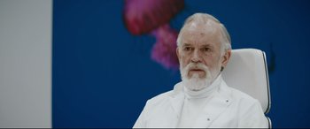 Movie still from “Journal 64” (2018), directed by Christoffer Boe – An old man with a beard and a white jacket; Medium shot, Low angle