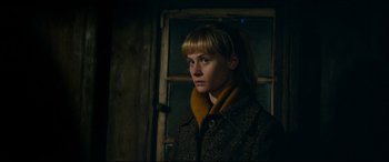 Movie still from “Journal 64” (2018), directed by Christoffer Boe – A young woman in a brown coat standing in front of a window; Close Up shot, Low angle