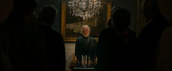 Movie still from “Journal 64” (2018), directed by Christoffer Boe – An older man standing in front of a painting; Medium shot, Over the shoulder angle