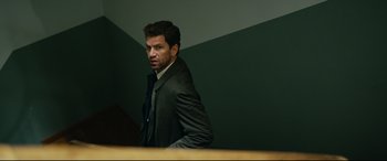 Movie still from “Journal 64” (2018), directed by Christoffer Boe – A man in a suit standing in front of a wooden table; Medium shot, Low angle