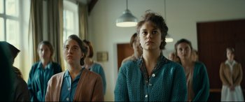 Movie still from “Journal 64” (2018), directed by Christoffer Boe – A group of people standing in a room; Medium shot, Low angle