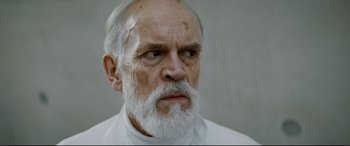 Movie still from “Journal 64” (2018), directed by Christoffer Boe – An old man with a beard and a white shirt; Close Up shot, Low angle