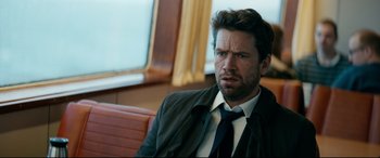 Movie still from “Journal 64” (2018), directed by Christoffer Boe – A person wearing a suit and tie; Close Up shot, Over the shoulder angle