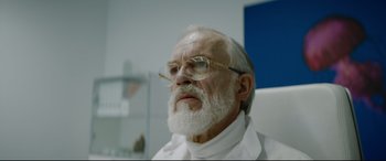 Movie still from “Journal 64” (2018), directed by Christoffer Boe – An older man with a beard and glasses; Close Up shot, Low angle