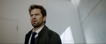 Movie still from “Journal 64” (2018), directed by Christoffer Boe – A person wearing a suit and a tie; Close Up shot, Over the shoulder angle