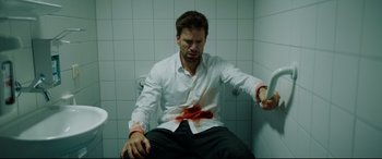 Movie still from “Journal 64” (2018), directed by Christoffer Boe – A man sitting in a bathroom with blood on his face; Medium shot, Overhead angle