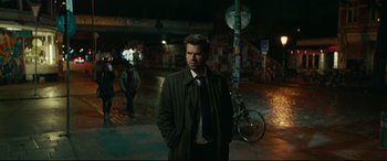 Movie still from “Journal 64” (2018), directed by Christoffer Boe – A man standing on the street at night with his hands in his pockets; Medium shot, Over the shoulder angle