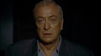 Movie still from “The Quiet American” (2002), directed by Phillip Noyce – An older man in a black jacket and blue shirt; Close Up shot, High angle