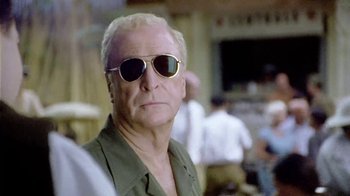 Movie still from “The Quiet American” (2002), directed by Phillip Noyce – An older man wearing sunglasses and a green shirt; Close Up shot, Over the shoulder angle
