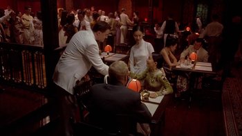 Movie still from “The Quiet American” (2002), directed by Phillip Noyce – A group of people sitting at a table in a restaurant; Wide shot, Over the shoulder angle