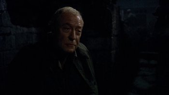 Movie still from “The Quiet American” (2002), directed by Phillip Noyce – An older man in a dark room looking at the camera; Close Up shot, Over the shoulder angle