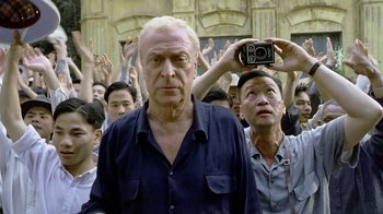 Movie still from “The Quiet American” (2002), directed by Phillip Noyce – An older man is standing in front of a group of people; Medium shot, Low angle