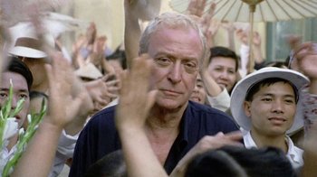 Movie still from “The Quiet American” (2002), directed by Phillip Noyce – An older man with white hair is in a crowd of people; Close Up shot, Over the shoulder angle