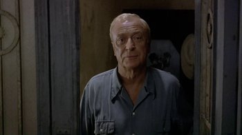 Movie still from “The Quiet American” (2002), directed by Phillip Noyce – An older man wearing a blue shirt and looking at the camera; Close Up shot, Low angle