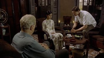 Movie still from “The Quiet American” (2002), directed by Phillip Noyce – A group of people sitting around a living room table; Wide shot, Over the shoulder angle