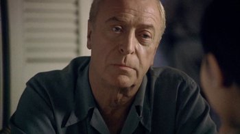 Movie still from “The Quiet American” (2002), directed by Phillip Noyce – An older man with a goatee looking at the camera; Close Up shot, Over the shoulder angle