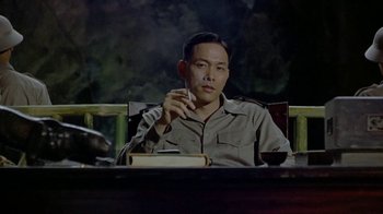 Movie still from “The Quiet American” (2002), directed by Phillip Noyce – A man sitting at a table with a book in front of him; Medium shot, Low angle