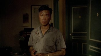 Movie still from “The Quiet American” (2002), directed by Phillip Noyce – A man in a gray shirt is standing in a room; Medium shot, Low angle